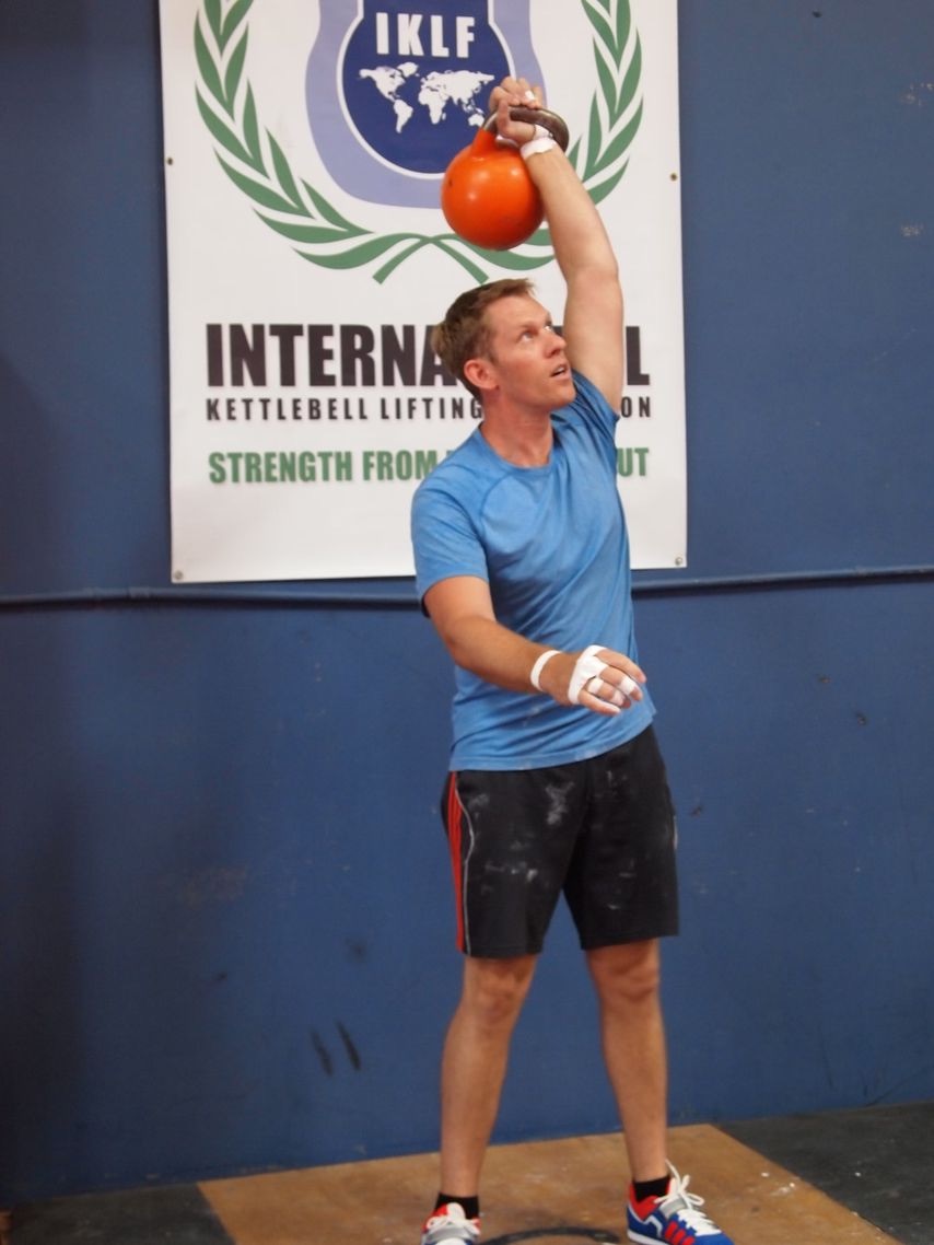 Cody Bramlett lifting a kettlebell overhead in his gym years