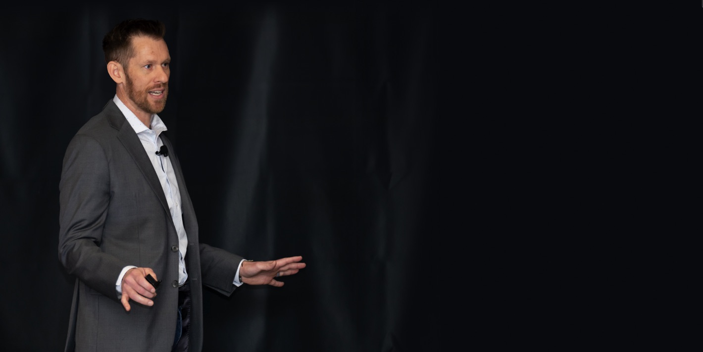 Cody Bramlett speaking on stage in a gray suit