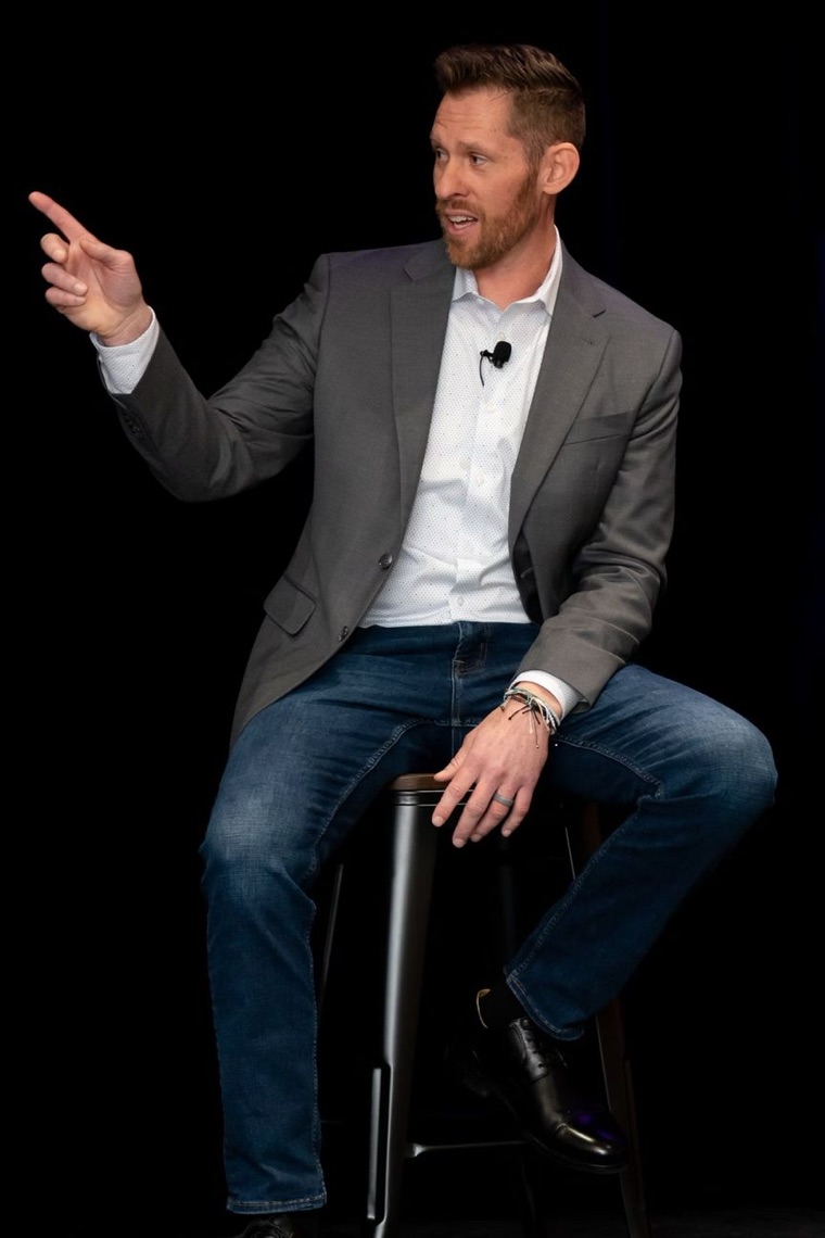 Cody Bramlett on stage, seated on a stool and pointing to the audience
